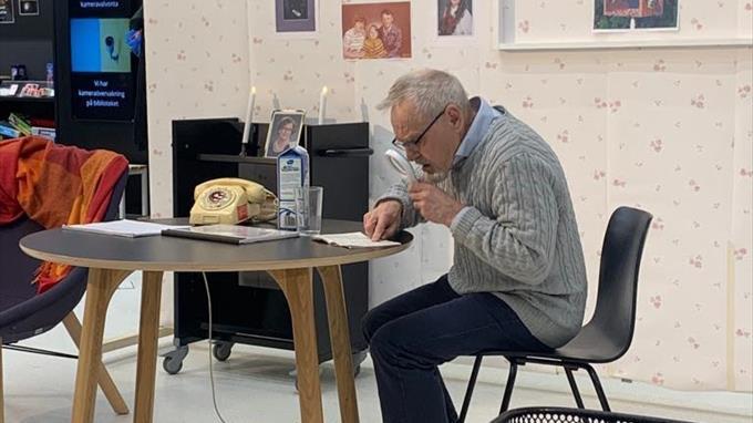 Vanha mies tutkii suurennuslasia tekstiä pöydän ääressä