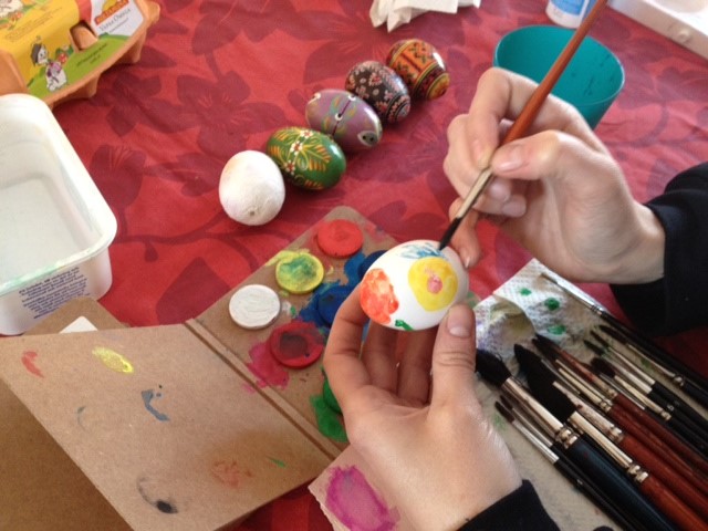 Pöydällä erilaisia maalausvälineitä, kananmunaan ollaan maalaamassa siveltimellä kuvioita.
