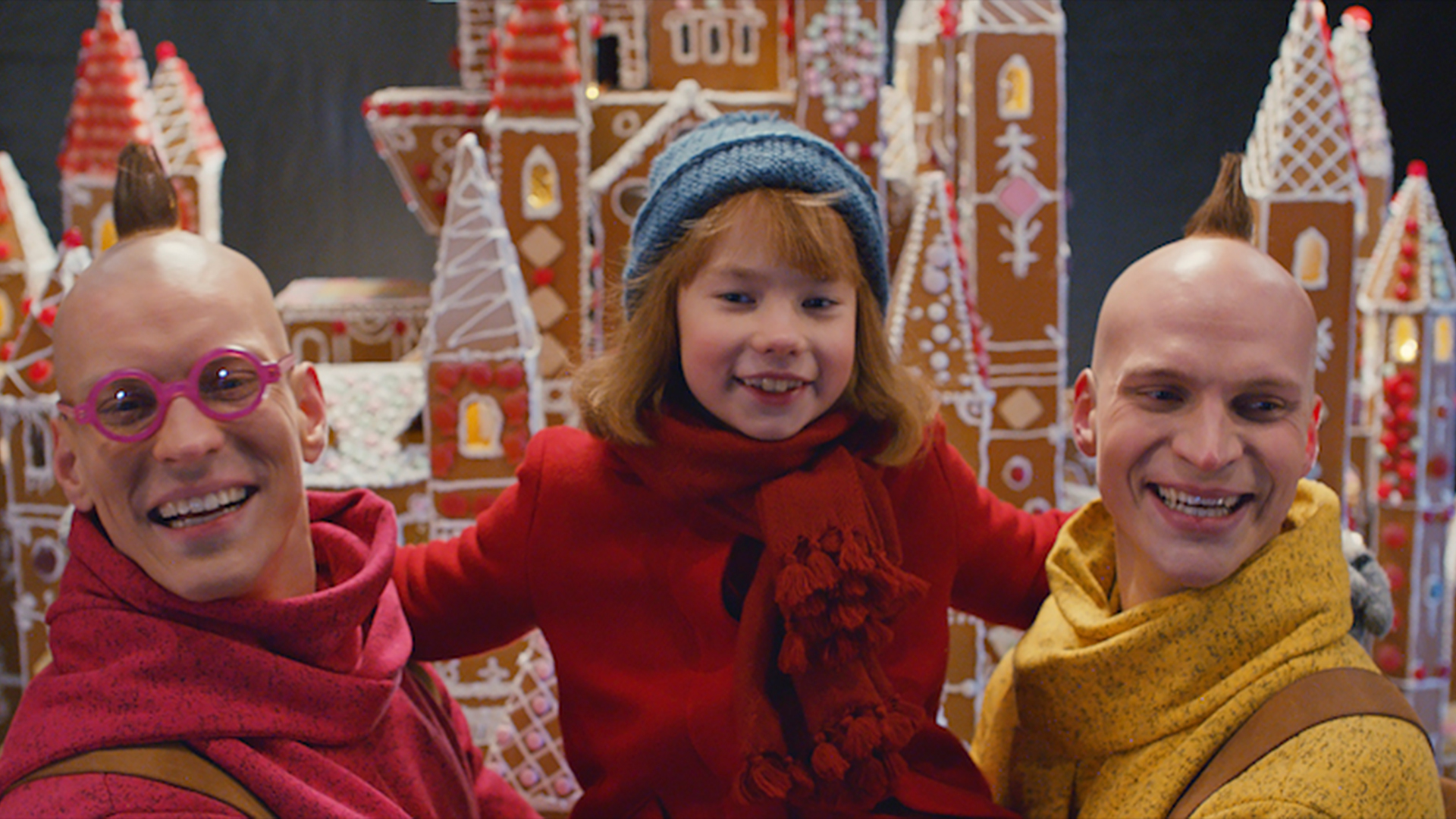 Tatu ja Patu (näyttelijät Riku Nieminen ja Antti Holma) halaavat lapsiystäväänsä Veeraa, taustalla iso piparkakkutalo.