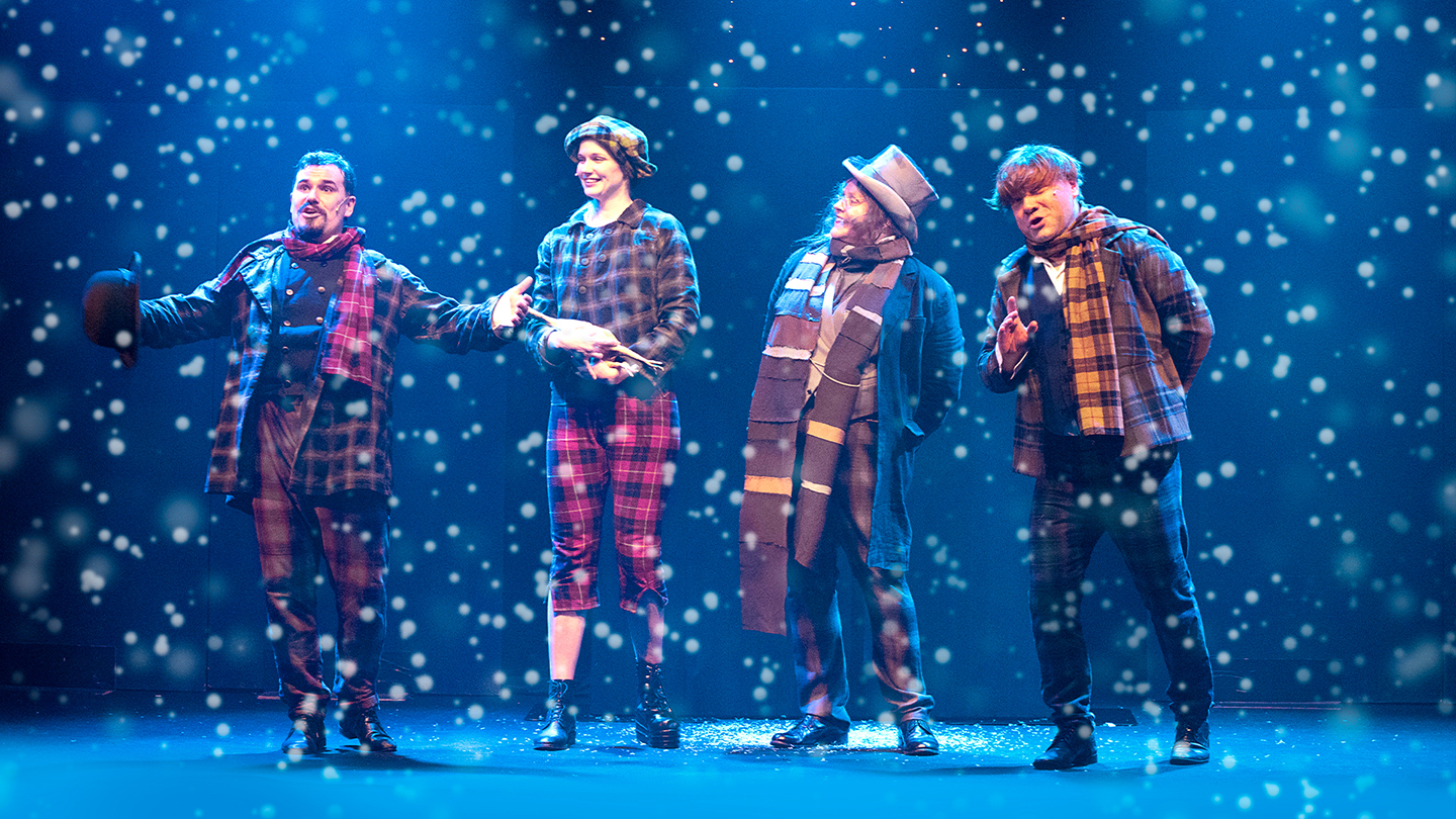 Neljä henkilöä seisoo näyttämöllä laulaen lumisateessa.