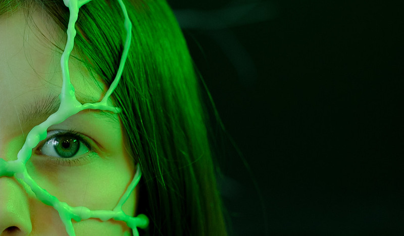Vihreällä värillä valaistu nuoren naisen kasvot, jonka päällä kasvaa sienirihmastoa.
