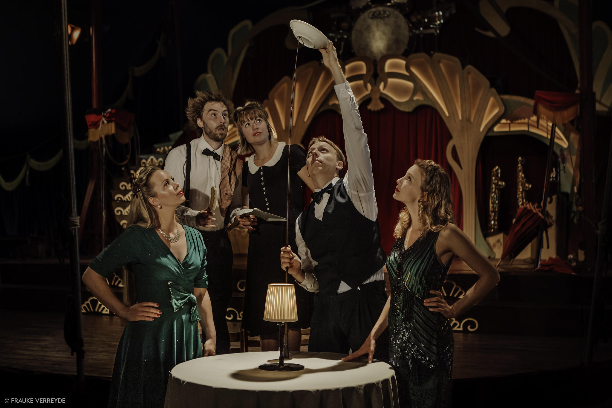 Ryhmä sirkusesiintyjiä katsoo ihmetellen, kun nuori esiintyjä tasapainottelee lautasta pitkän tikun päässä.