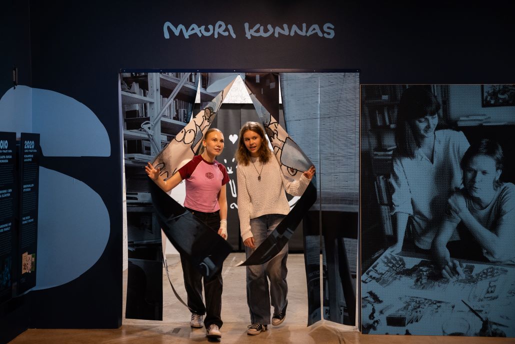 Kaksi tyttöä astumassa Mauri Kunnas -näyttelyn huoneeseen