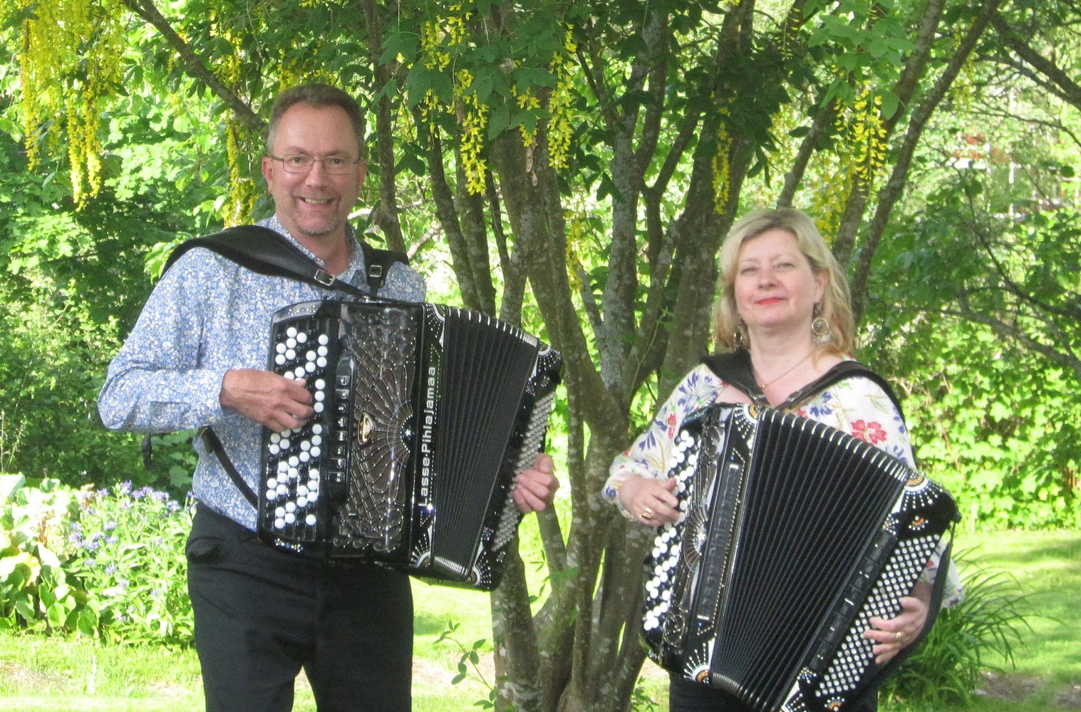 Pekka Pentikäinen ja Maria Kalaniemi soittavat harmonikkaa puun alla. Dragspelarna Pekka Petikäinen och Maria Kalaniemi under ett träd.