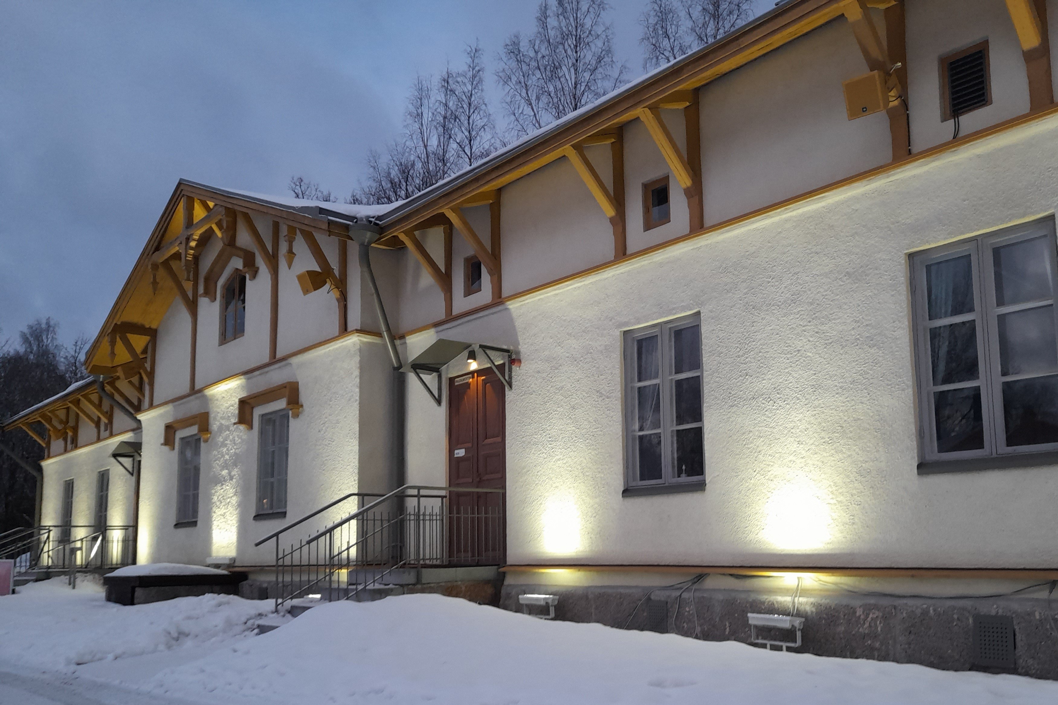Kuvassa Lasten kulttuurikeskus Auroran julkisivu kuvattuna talvi-iltana. Talon julkisivu on valaistu, taivas on pilvinen ja maassa on lunta.
