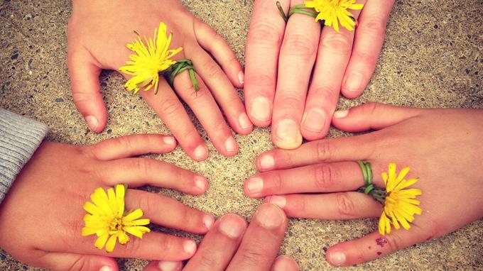 Eri kokoisia käsiä, joissa kukka sormien välissä.