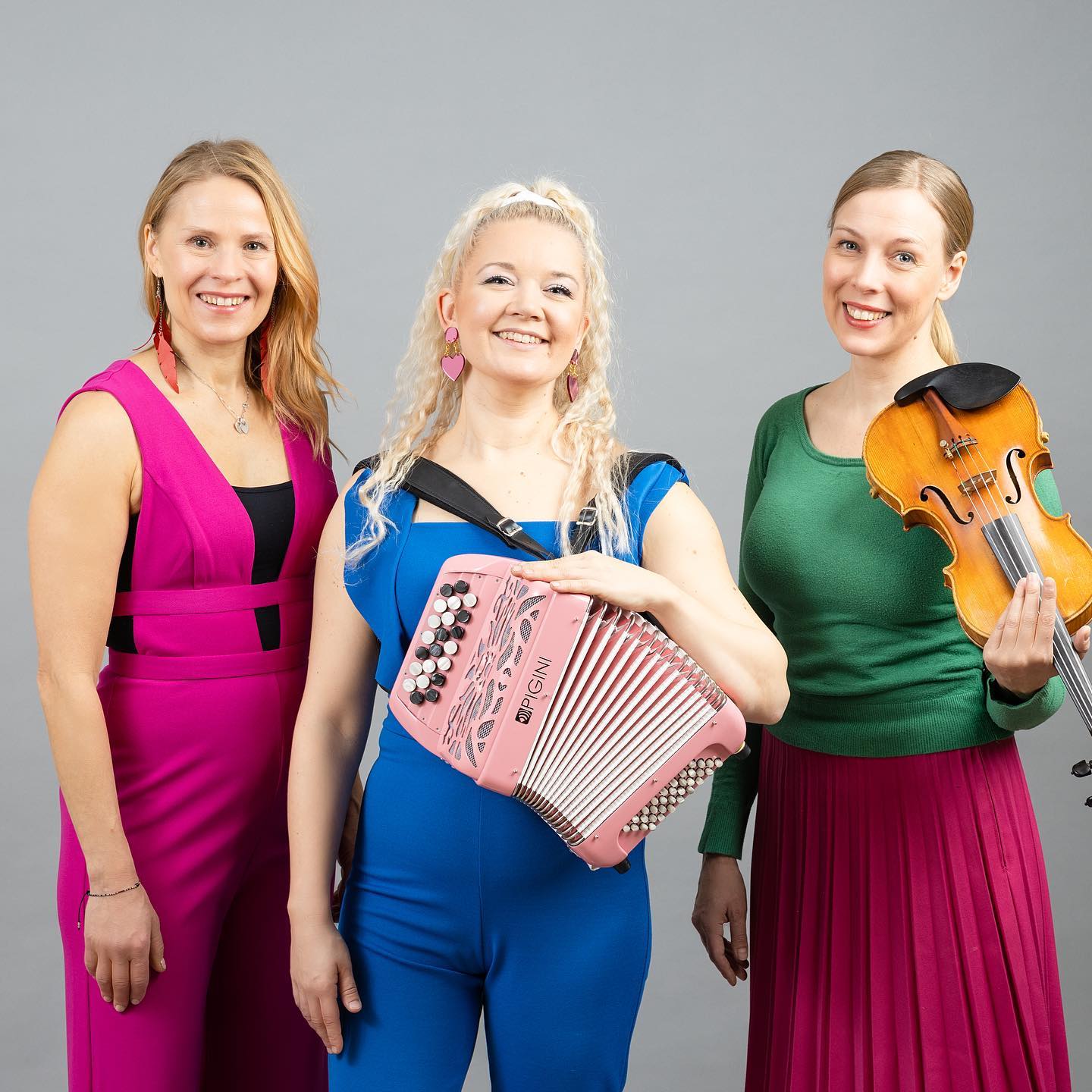 Kolme naista, keskimmäisellä on vaaleanpunainen pikkuhaitari ja oikeanpuoleisella viulu.