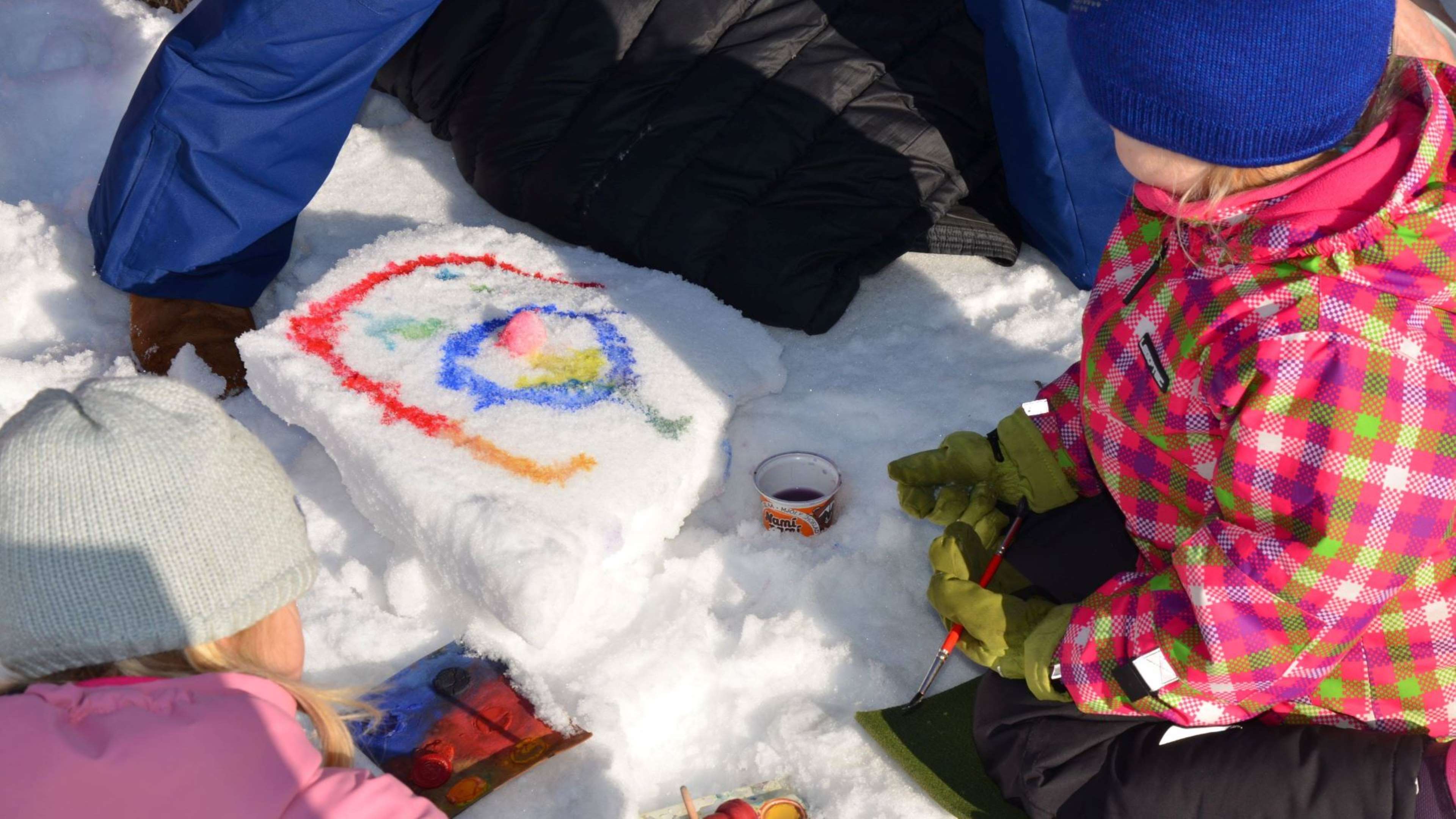 Lapset maalaa vesiväreillä lumeen kuvioita.
